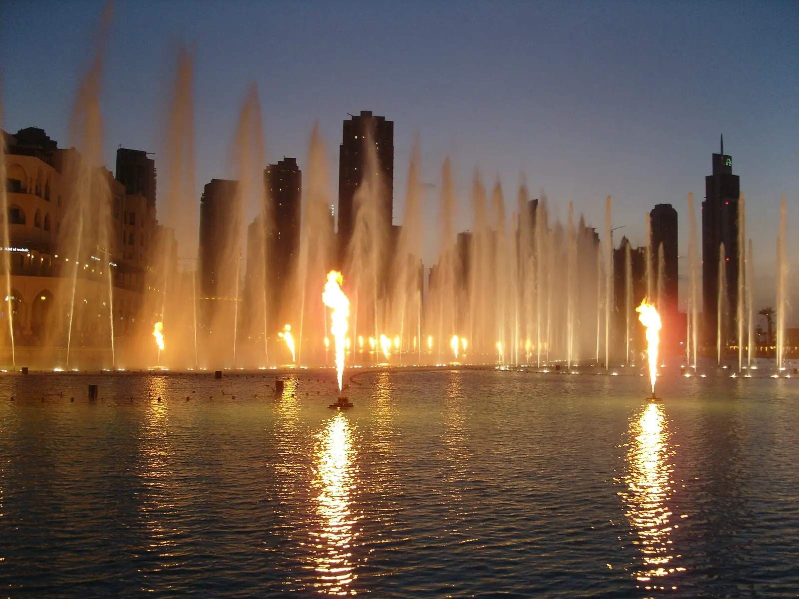 The Dubai Fountain lit up at night in front of the Downtown towers